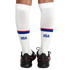 Rear view of a person's legs wearing white knee-high USA socks with red and blue stripes and black Nike Phantom soccer shoes.