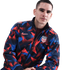 A man with freckles wears a red and blue geometric Nike USA national soccer team jacket against a white background.
