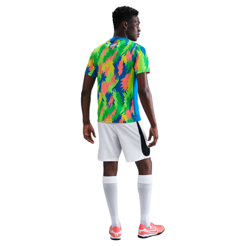 Rear view of a Black man in a colorful patterned jersey, white shorts, long white socks, and pink sneakers against a plain white background.