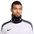 Close-up of a man wearing a black Nike neck gaiter and a white Nike athletic shirt against a black background.