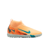 A bright orange Nike soccer turf shoe with teal accents, a sock-like collar, and "KM" logo on the heel, shown against a solid black background.