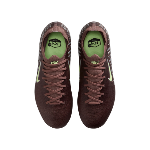 Overhead view of deep burgundy Nike soccer cleats with pale green accents and "KM" branding, set against a black background.