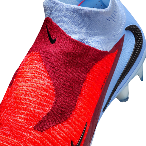Close-up of a red and light blue Nike soccer boot featuring a textured Gripknit upper, black Nike swoosh, and a laceless ankle collar.