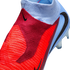 Close-up of a red and light blue Nike soccer boot featuring a textured Gripknit upper, black Nike swoosh, and a laceless ankle collar.
