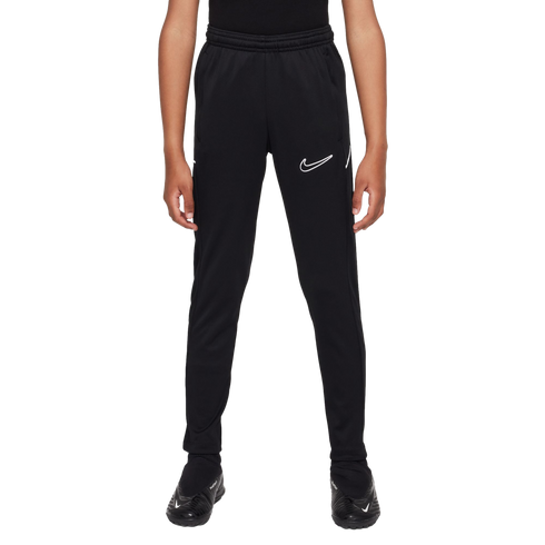 A person wearing black Nike athletic pants with a white swoosh outline on the left thigh and black soccer cleats against a white background.