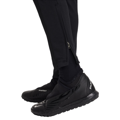 Close-up of a person wearing all-black Nike athletic gear, including Phantom GT turf shoes, socks, and tapered pants with ankle zippers.