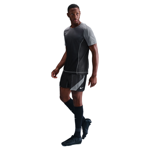 A man poses in a grey and black Nike soccer kit, featuring a short-sleeve jersey, matching shorts, and black cleats, set against a solid black background.