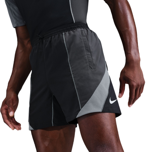 Close-up of a person wearing black Nike athletic shorts with grey mesh panels and a white swoosh logo against a solid black background.