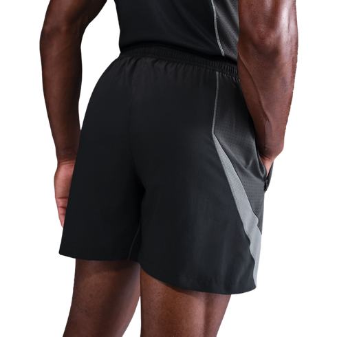Rear view of a person wearing black athletic shorts with grey mesh side panels and a matching black tank top against a black background.