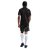 Back view of a man with braided hair wearing a black soccer jersey, patterned shorts, tall white socks, and black cleats.