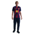 A blonde man wearing an FC Barcelona football jersey, navy track pants, and black trainers, standing against a solid black background.
