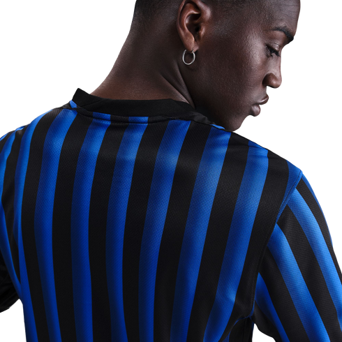 Close-up of a person with dark skin from behind, wearing a blue and black striped jersey and a silver hoop earring.