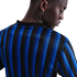 Close-up of a person with dark skin from behind, wearing a blue and black striped jersey and a silver hoop earring.