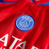 Close-up of a red Paris Saint-Germain soccer jersey featuring the team's blue circular crest, a partial blue Nike swoosh, and white text.