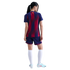 Rear view of a woman in a red and blue striped soccer kit, white socks, and light blue cleats against a black background.