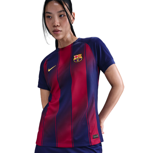 A woman wearing a navy blue and red striped FC Barcelona soccer jersey with a yellow Nike swoosh and club crest, posed against a black background.