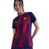 A woman wearing a navy blue and red striped FC Barcelona soccer jersey with a yellow Nike swoosh and club crest, posed against a black background.