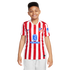 A smiling young boy wearing a red and white striped Atlético Madrid soccer jersey and light grey shorts, standing against a plain white background.