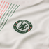 Close-up of a green Chelsea Football Club crest on a white textured jersey with thin red and green diagonal stripes in the corner.