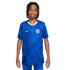 A young boy with braided hair smiling while wearing a blue Nike Chelsea FC football jersey against a plain white background.