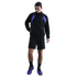 A man wearing a black tracksuit jacket with purple shoulder panels, black shorts, and purple sneakers against a solid black background.
