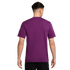 Rear view of a man wearing a plain purple short-sleeved t-shirt and black shorts against a solid black background.