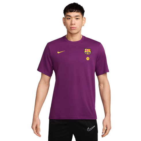 A young man models a purple short-sleeve FC Barcelona t-shirt with gold Nike and Spotify logos, and club crest, paired with black Nike shorts.