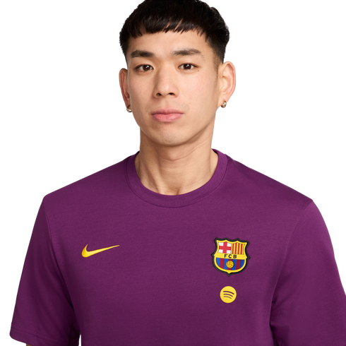 Headshot of a person with short dark hair wearing a purple Nike FC Barcelona t-shirt with the team crest and a Spotify logo, against a solid black background.