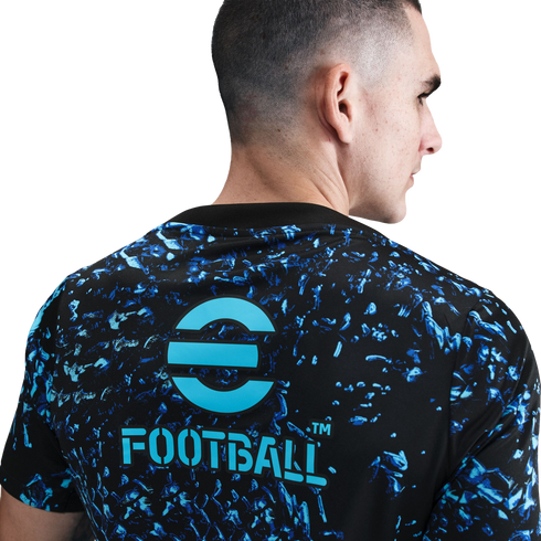 Rear view of a man wearing a black t-shirt with a blue abstract print and the light blue eFootball logo on the back. He faces right against a white background.