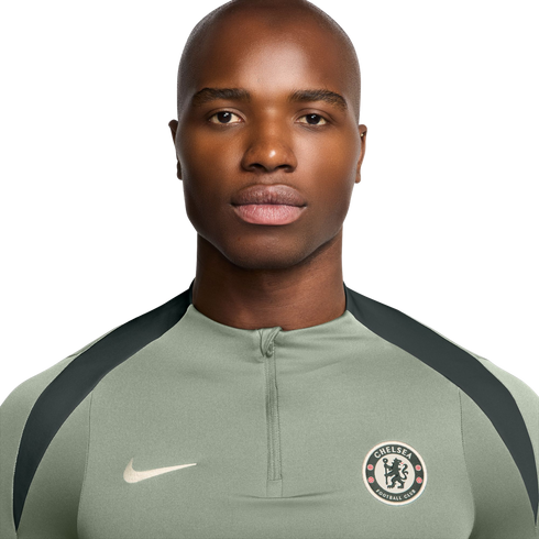 Headshot of a bald man wearing a sage green Nike quarter-zip shirt with a Chelsea FC crest against a white background.