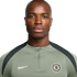 Headshot of a bald man wearing a sage green Nike quarter-zip shirt with a Chelsea FC crest against a white background.