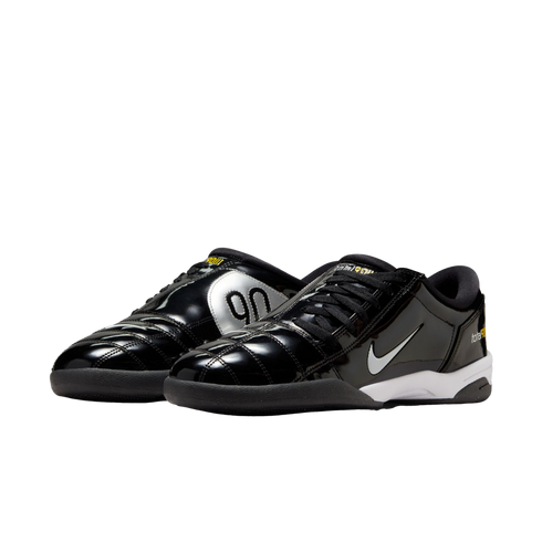 A pair of glossy black Nike Total 90 indoor soccer shoes with silver "90" branding, white swooshes, and yellow accents, shown against a white background.