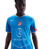A man with a serious expression wears a light blue Nike soccer jersey with the Atletico Madrid crest and Riyadh Air logo, set against a solid black background.