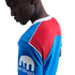 A person wearing a blue and red athletic jersey with a white 'Kraken' logo on the sleeve, looking down against a black background.