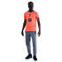 A man modeling a bright orange Nike FC Barcelona jersey, grey athletic pants, and black sneakers against a black background.