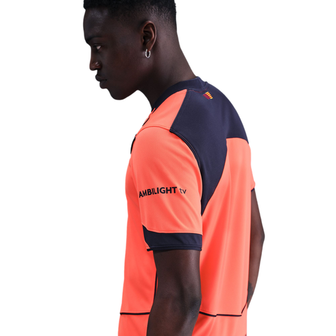 Profile of a man wearing a bright orange and navy blue athletic shirt with "AMBILIGHT tv" on the sleeve, set against a solid black background.