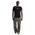 Man wearing a black Nike Chelsea FC jersey, camouflage cargo pants, and gold metallic sneakers against a black background.