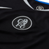 Close-up of a black Chelsea FC jersey with a white embroidered circular lion crest and "CFC" lettering. The collar features blue and white trim and a "90" logo inside.