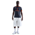 A man wearing a grey and orange Inter Milan training jersey, white knee-length shorts, and white sneakers, standing against a solid black background.