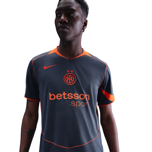 A man wearing a grey and orange Nike Inter Milan soccer jersey with a Betsson.sport logo, looking to the side against a black background.