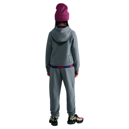 Rear view of a person wearing a grey tracksuit, a magenta beanie, and colorful patterned sneakers against a solid black background.