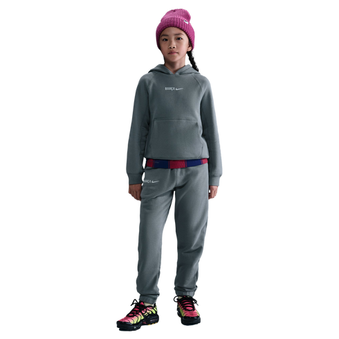 Child in a gray Nike FC Barcelona tracksuit, pink beanie, and colorful sneakers against a black background.