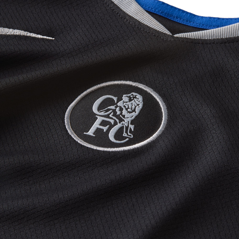 Close-up of a black Chelsea FC jersey featuring a silver embroidered crest with a lion and 'CFC' initials, a white Nike swoosh, and a collar with blue and grey trim.