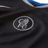 Close-up of a black Chelsea FC jersey featuring a silver embroidered crest with a lion and 'CFC' initials, a white Nike swoosh, and a collar with blue and grey trim.