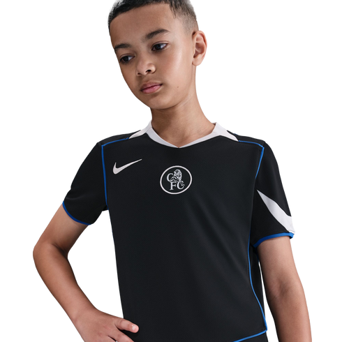 A boy wears a black Nike Chelsea FC soccer jersey with blue trim and a white crest, looking down against a plain black background.