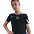 A boy wears a black Nike Chelsea FC soccer jersey with blue trim and a white crest, looking down against a plain black background.