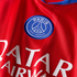 Close-up of a red Paris Saint-Germain football jersey featuring the club's blue circular crest and white sponsor text.
