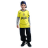 A smiling boy in a yellow Tottenham Hotspur jersey, grey long-sleeved shirt, navy cap, and dark pants, standing against a black background.