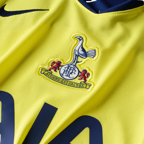 Close-up of a yellow Tottenham Hotspur football jersey featuring the club's embroidered crest and a dark blue Nike swoosh.