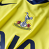 Close-up of a yellow Tottenham Hotspur football jersey featuring the club's embroidered crest and a dark blue Nike swoosh.